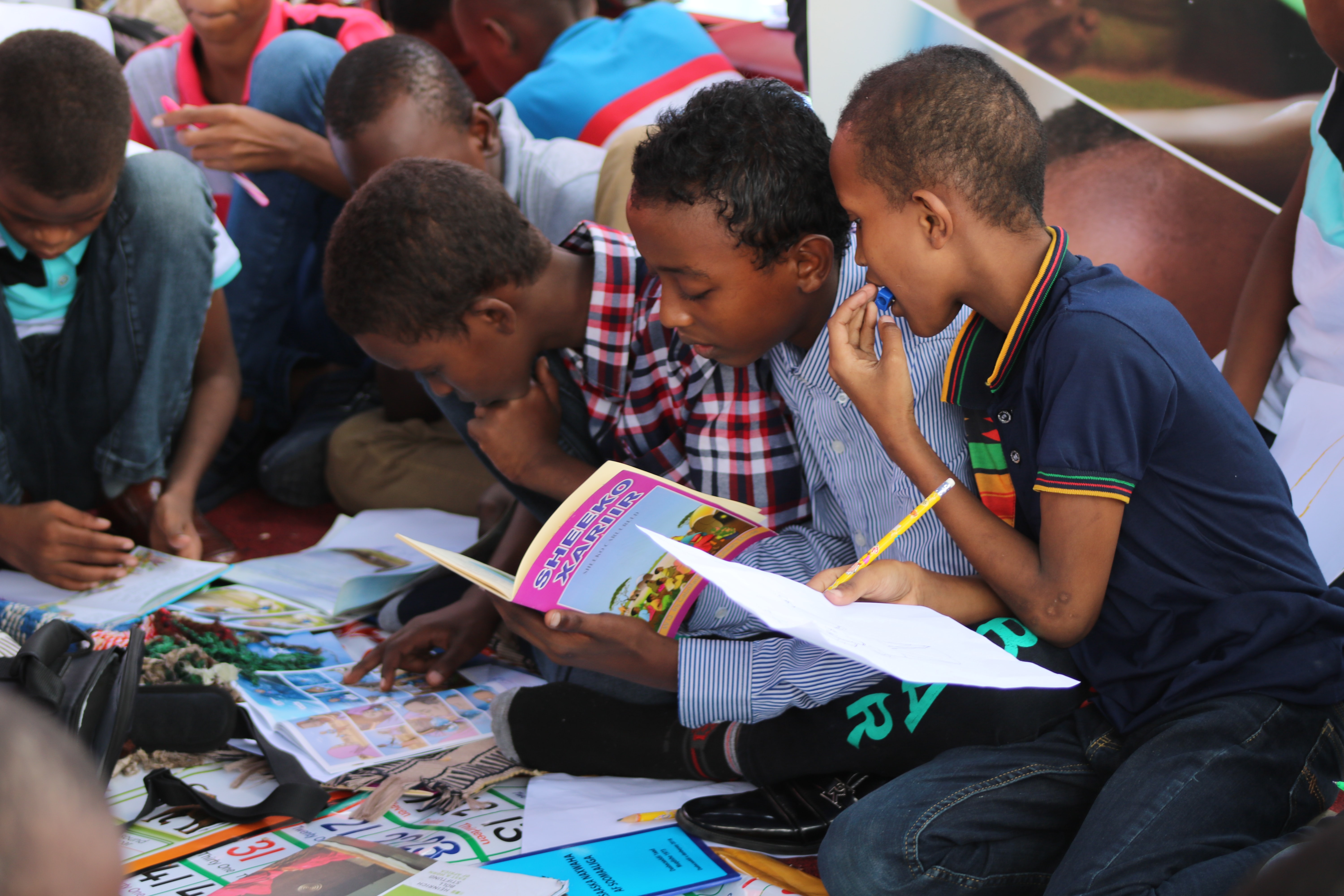 children gathered around a book titled SHEEKO XARIIR